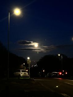 cars are parked on the side of the road at night with street lights in the background