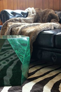 a green table sitting on top of a black leather couch next to a zebra print rug