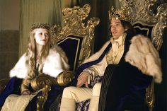 a man and woman dressed in period costumes sitting on gold thrones with fur stolers