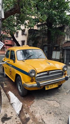 an old yellow taxi cab is parked on the side of the road next to a tree