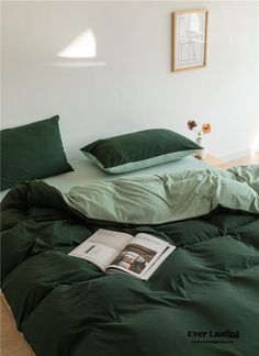 a bed with green sheets and pillows on top of it, next to a book