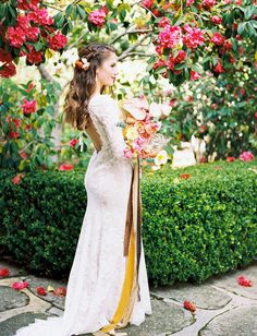 a woman in a white dress is holding flowers and posing for the camera with her back to the camera