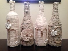 three wine bottles made out of rope with flowers on the front and side, sitting next to each other