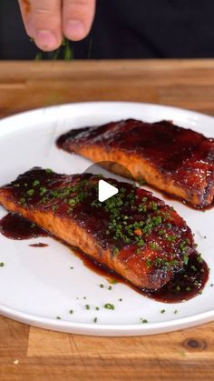 two salmon fillets on a white plate with red sauce and green garnish