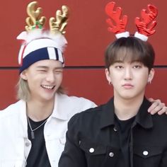 two young men with reindeer antlers on their heads posing for a photo in front of a red wall