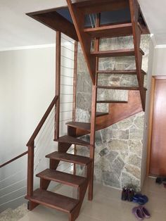 there is a wooden stair case next to the wall and shoes on the floor in front of it