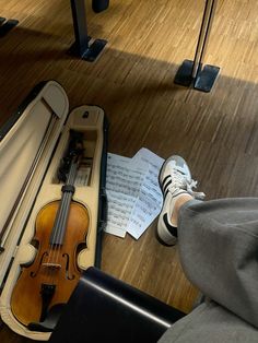 a violin and some sheet music on the floor next to a person's feet