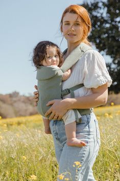 a woman holding a baby in her arms while standing in a field with yellow flowers