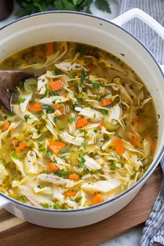 chicken noodle soup in a white pot with a wooden spoon and text overlay