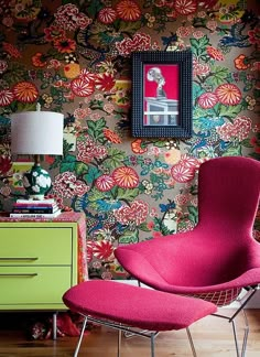 a pink chair sitting in front of a wall with flowers on it and a green dresser