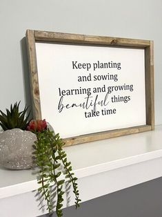 a plant is sitting on top of a shelf next to a framed sign that says keep planting and sowing learning and growing beautiful things take time