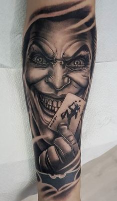 a man with a joker tattoo on his leg holding a playing card in one hand