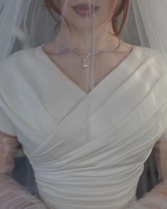 a woman in a white dress with a veil over her head and wearing a diamond necklace