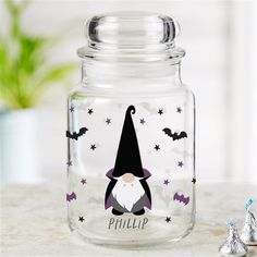 a glass jar with an image of a gnome and bats on the lid, next to herspooos