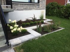 a small garden with white flowers in the grass next to a brick wall and stairs