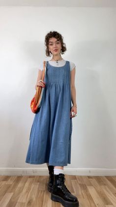 a woman standing in front of a white wall wearing a blue dress and black boots