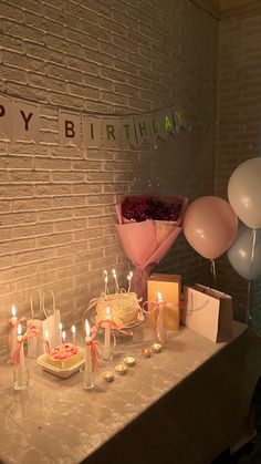 a birthday party with balloons, cake and gifts on a table in front of a brick wall