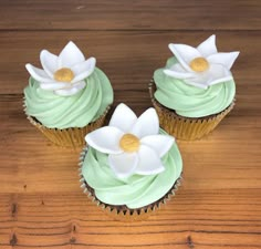 three cupcakes with green frosting and white flowers on them sitting on a wooden table