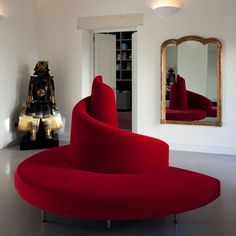 a red couch sitting in the middle of a living room next to a large mirror