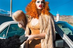 a woman with red hair is standing next to a car and petting a dog