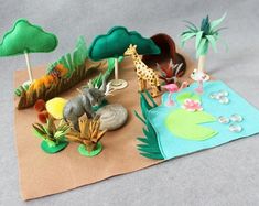 an assortment of toy animals sitting on top of a piece of paper next to trees and rocks