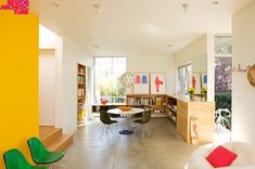 a living room filled with lots of furniture next to a yellow wall and bookshelf