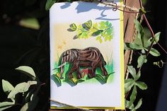 a card with an image of a rhino on it hanging from a tree in front of some leaves