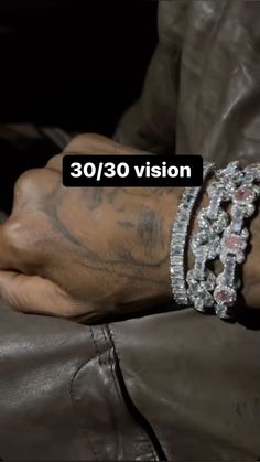 a person with tattoos and bracelets on their wrist, wearing a leather jacket that says 30 / 30 vision