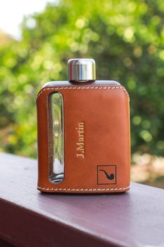 a leather flask with a lighter in it on a wooden table next to trees