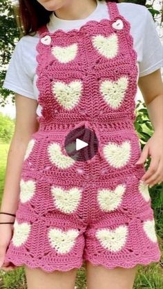 a woman wearing pink and white crocheted overalls with hearts on the front