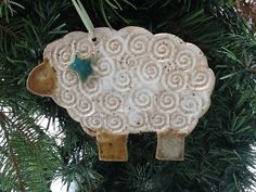 a ceramic sheep ornament hanging from a christmas tree with green leaves on it