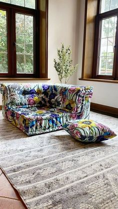 a colorful couch sitting on top of a rug in front of two large windows with wooden frames