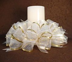 a white candle with gold ribbon around it sitting on a table next to a brown background