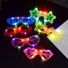 four flashing glasses with bows and lights on top of a black table next to an open book