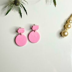 pink and white earrings with pearls hanging from them on a table next to some plants