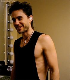 a man standing in front of a mirror with ear buds on his ears and wearing a black tank top