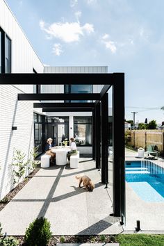 a dog laying on the ground in front of a swimming pool and covered patio area