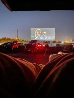 a movie screen in the middle of a parking lot with cars parked around it at night