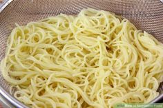 a bowl filled with noodles sitting on top of a wooden table next to a metal strainer