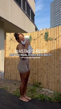 a woman standing in front of a bamboo fence holding a white cup with the words diastasis erect on it