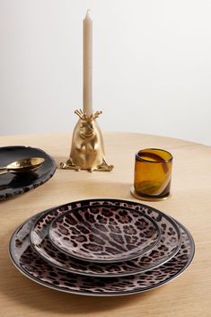 a wooden table topped with black and brown plates next to a lit candle on top of it