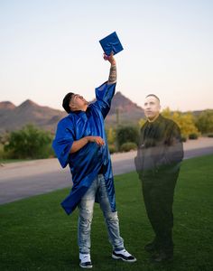 a man in a blue graduation gown is holding up his cap and looking up at the sky