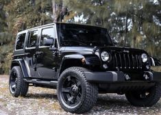 a black jeep parked on the side of a dirt road in front of some trees