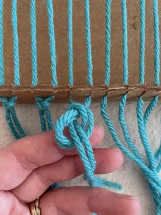 a person is holding a piece of blue yarn in front of a cardboard box that has two strings attached to it