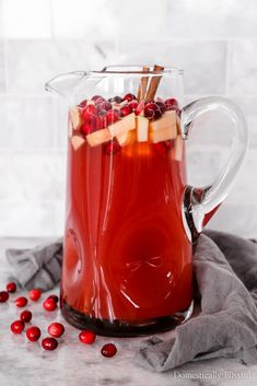 a pitcher filled with red liquid and apples on top of a marble table next to some cranberries