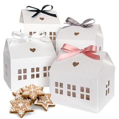 three white boxes with gingerbread cookies in the shape of houses and snowflakes