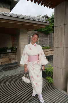 a woman in a white and pink kimono is standing on the ground with her handbag