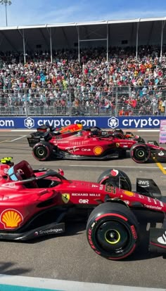 three red race cars in front of a large crowd