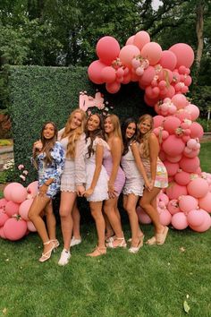 a group of women standing next to each other in front of a pink balloon arch