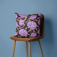 a purple flowered pillow sitting on top of a wooden chair next to a blue wall